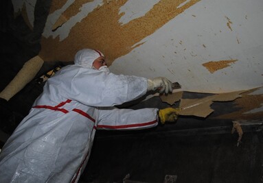 Person in Schutzanzug entfernt alte Tapete von einer Wand.